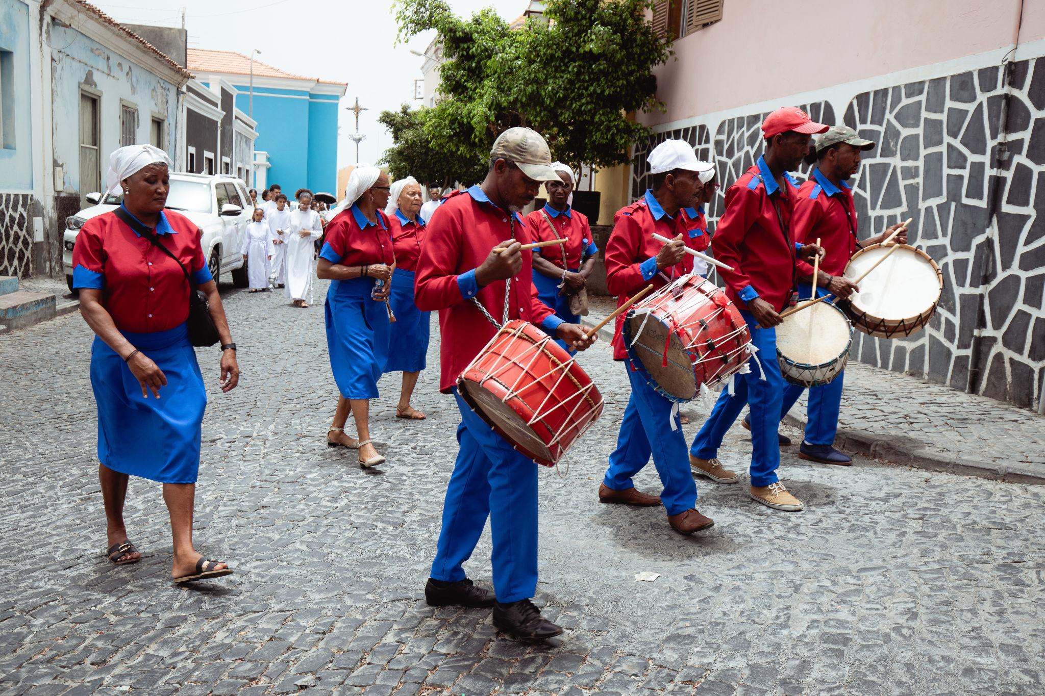 Traditional Cape Verde drummers in red and blue uniforms performing in a cobblestone street procession